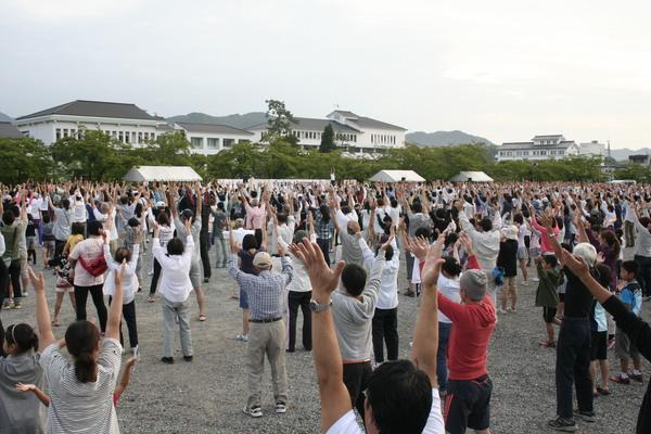 両手を挙げている沢山の老若男女の後ろからの写真