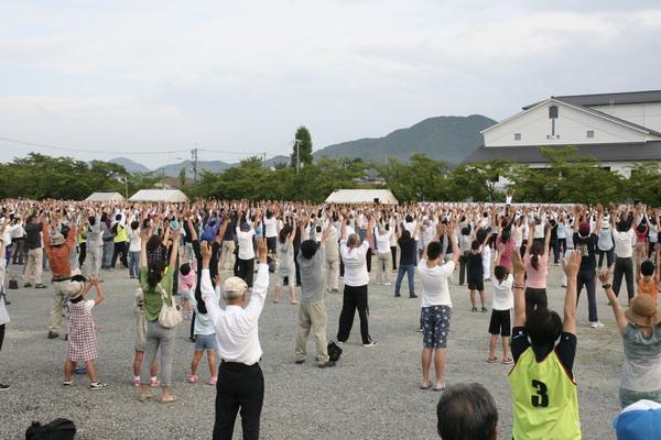斜め後ろからの両手を上げる体操をする老若男女の写真