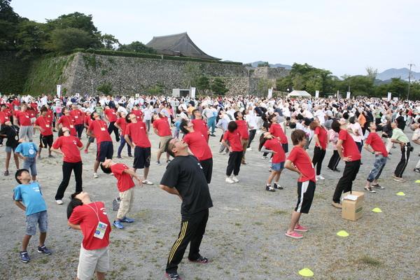 腰に手をあて、体をそらす体操をする老若男女の写真