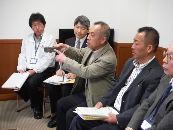 男性5名が椅子に座り、そのうちの一人が陶器を手に持ち説明をしている様子の写真