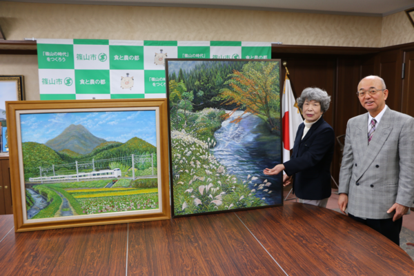 2まいの油絵を手で指している赤井 寿美さんと市長が一緒に写っている写真