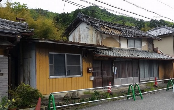 老朽化で屋根瓦が波打っている空き家の前に工事用三角コーンなどが置かれている写真