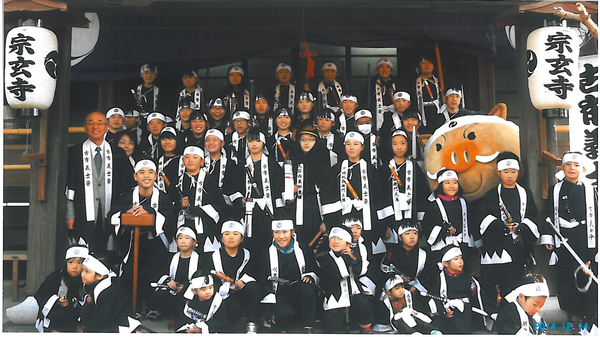 宗玄寺の前で子ども義士行列に参加した子供たちと市長とまるいのが一緒に写っている集合写真