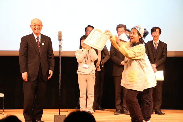 市長から渡された賞状を喜んで観客席の方に見せている写真