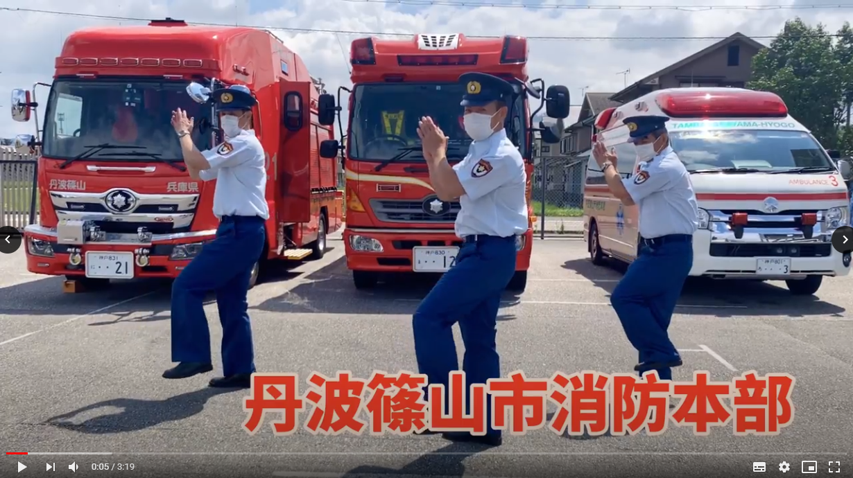 消防車、レスキュー車、救急車の前でデカンショ隊員3名がデカンショを踊っている