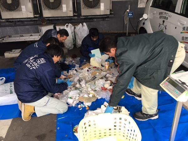 男性が回収してきたごみをブルーシートの上で分別している写真