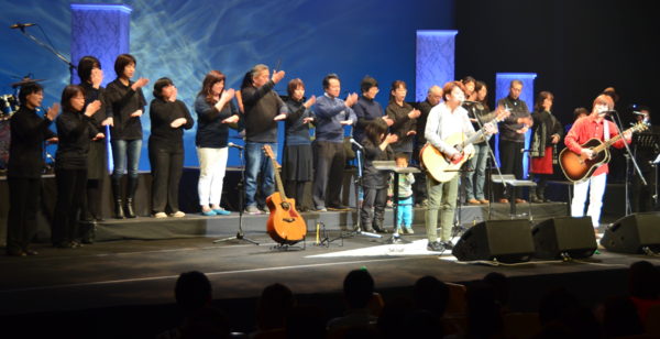 兄弟デュオ「ちめいど」がギターを持ち歌を歌っている後方で手話をしている手話サークルの方々の写真