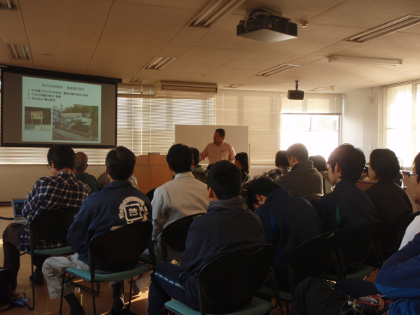 明かりが落とされた室内で、プロジェクトスクリーンを見る、聴衆者の写真