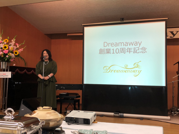 舞台上のスライドの横に立って話をしている吉田 真知子代表取締役社長の写真