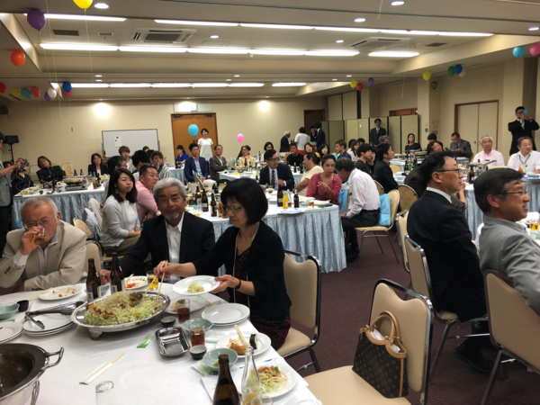 料理が並べられたそれぞれのテーブルにたくさんの人が着席している写真