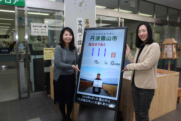 「丹波篠山市誕生まであと111日」と書かれたモニターの両脇に二人女性が立っていて、手でモニターを指してアピールしている写真