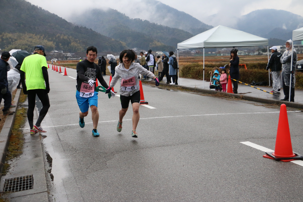 男性ランナーが、女性ランナーに緑のたすきを渡している写真