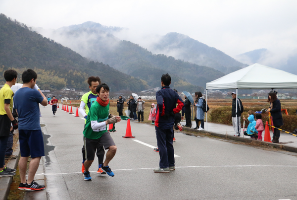 男性ランナーが、次の男性ランナーにたすきを渡し、走り出している写真