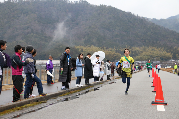 応援に来た観客たちが見守る中、黄色いユニ不フォームを着て走る男性ランナーの写真