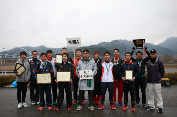 味間Aとかかれたプラカードを持ち、たくさんの額入りの賞状と、メダルを首にかけた男性ランナーの集合写真