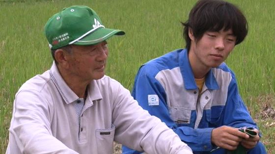 作業着を着た青年と、年配の男の人が座っている写真