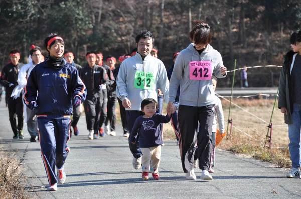 赤ハチマキの選手、黄緑ゼッケンの選手、ピンクのゼッケンの選手が子供の手を引いて走っている写真
