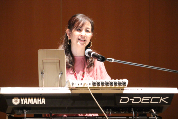 髪の長い女性が歌いながらキーボードを弾いている写真