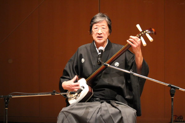 男性が歌いながら三味線を弾いている写真