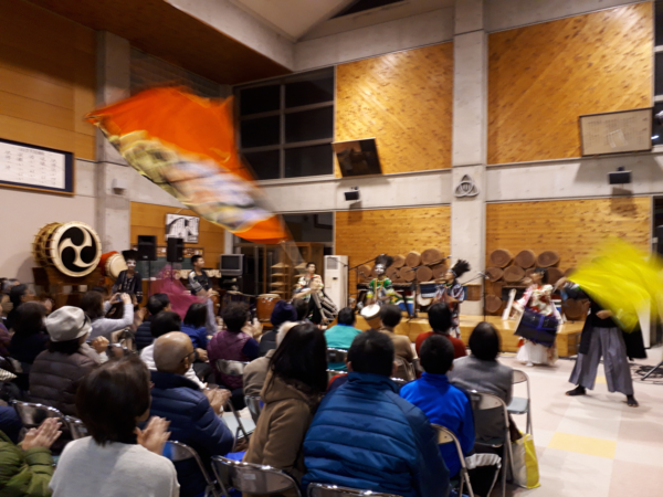 ジョセフ・ンコシさん達の演奏に「丹波篠山楽空間」のメンバーも加わって大きなオレンジ色と黄色の旗を振って演奏を盛り上げている様子の写真