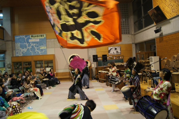 「丹波篠山楽空間」のメンバーが「楽」と書かれたオレンジ色の大きな旗を振って演奏を盛り上げている様子の写真