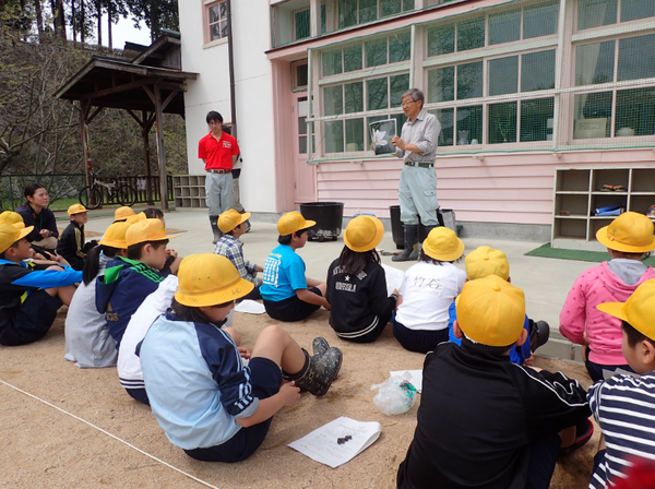 花蓮マイスターの金子 明雄さんがハスの花の写真を見せていて、聞いている児童の写真