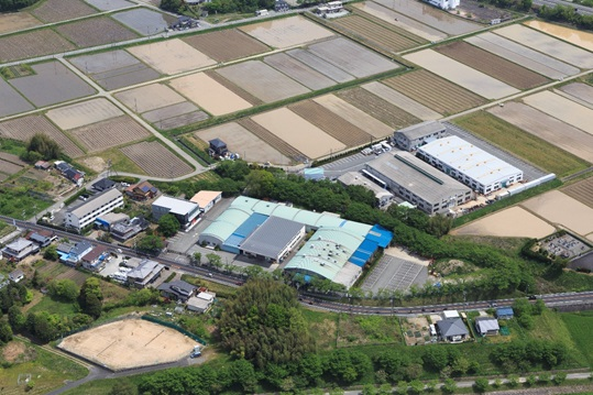 のどかな田園地帯が広がり工場敷地周辺に木が生い茂っている平和発條株式会社篠山工場を上から見た写真