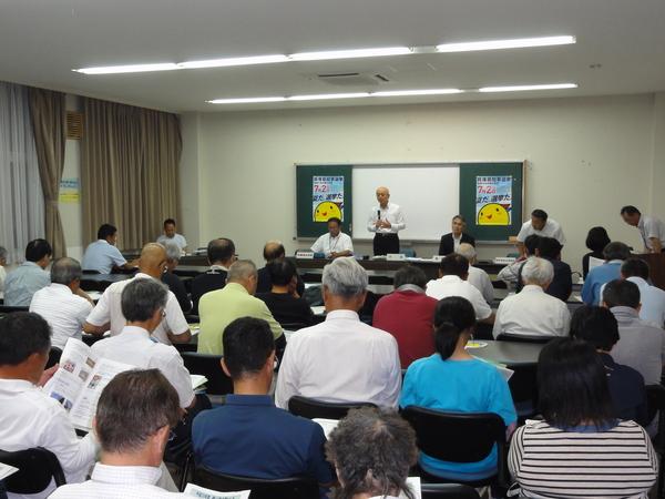 市長が立ち、マイクで話をしているのを参加者の方々が資料を見ながら話を真剣に聞いている後ろ姿の写真