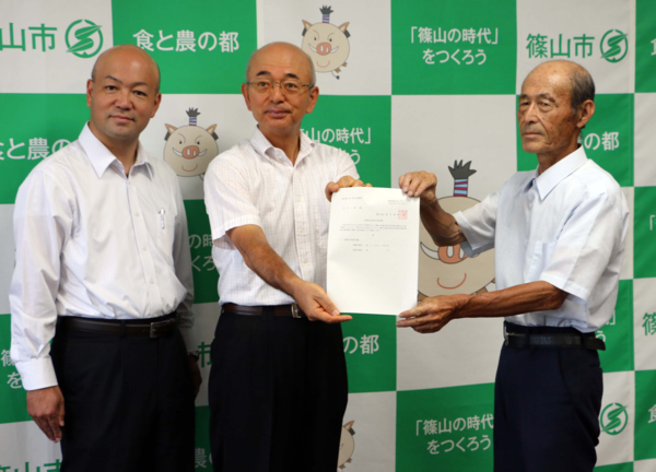 國里 修久議員の横で市長と本井 一寿さんが支援金支給決定通知書を持って写っている写真