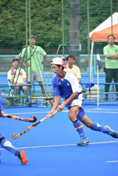 帽子をかぶった一名の選手がホッケーのスティックを持って、ボールを追いかけている写真