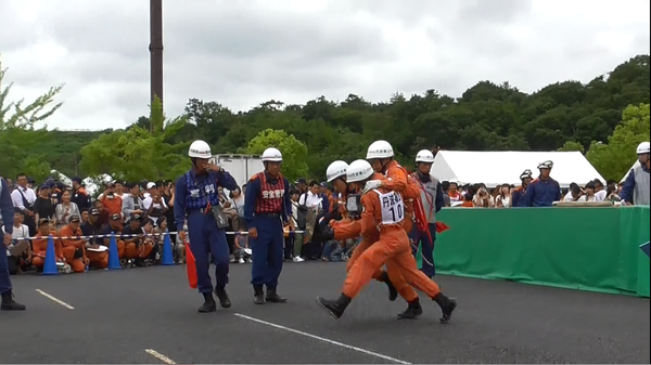 消防救助技術大会で救助者が技術者2名に運ばれているのを2名の審判員が見ている写真