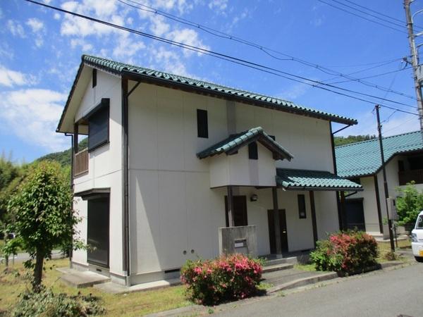 2階建てのクリーム色の外壁の家の玄関前につつじが咲いている写真