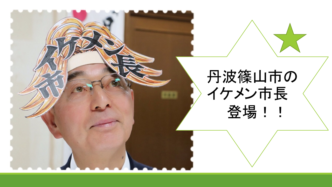 茶色のドアの前で紙で作られた茶色の髪の絵の上にイケメン市長と書かれた被り物を被った酒井市長が斜め上を向いている写真