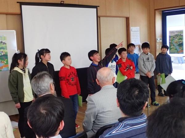 今田小学校のみなさんが前に出て発表しており、中央にいる男の子が左手を上に挙げて指差ししており、市長が前列で椅子に座って見ている様子の写真