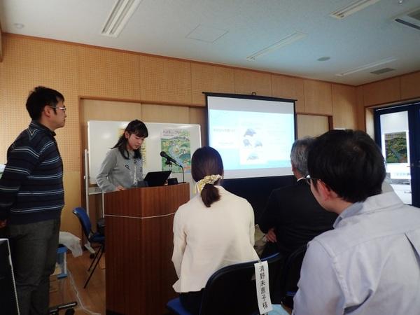 前方のスクリーンに映像が映されて、小嶋 優希さんが壇上に立って発表しており、その横でお父さんが発表の様子を見守っている様子の写真