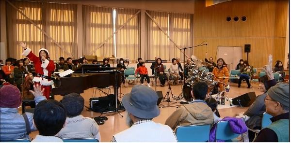 サンタ姿の吉田代表がマイクを持ち片手を広げお話ししている写真