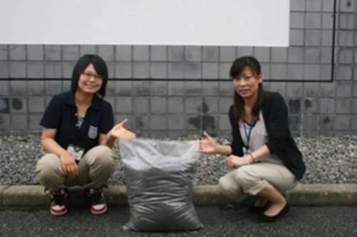 あさぎり乾肥が入った袋の両脇に女性職員がしゃがんで手のひらで袋を指している写真