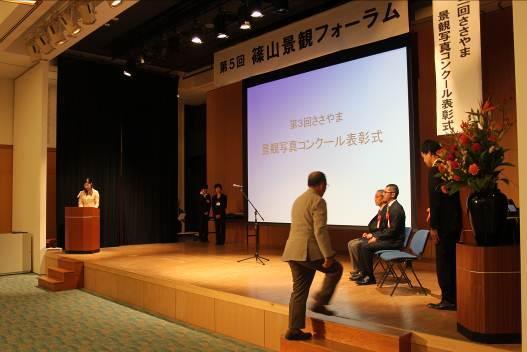 第3回ささやま景観写真コンクール表彰式で、三番目の受賞者の男性が舞台に上がっていく様子の写真