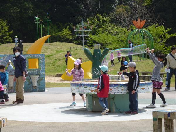 子供達が広場で遊んでいて、女の子が大きいシャボン玉を作っている写真