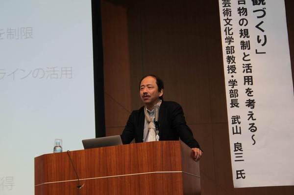 舞台上にて基調講演で話をしている武山 良三先生の写真