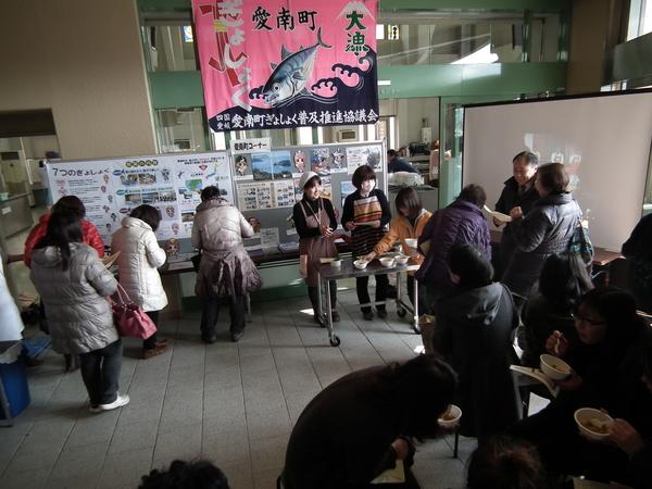 愛南町ぎょしょくの旗やパネルの展示されている会場で「愛南カツオカレー」が振舞われている写真