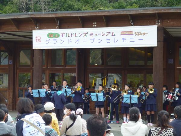 福住小学校の生徒みんなで起立し、トランペット・小太鼓・大太鼓を演奏している写真