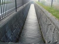 道路脇にある、小さな河川がコンクリートで3面張りされている様子の写真