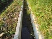 両脇には緑が生い茂っているが、コンクリートで作られたU字溝の写真