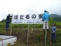 「ほたるの里」と書かれている看板を土手のようなところに、男性3名で設置している様子の写真
