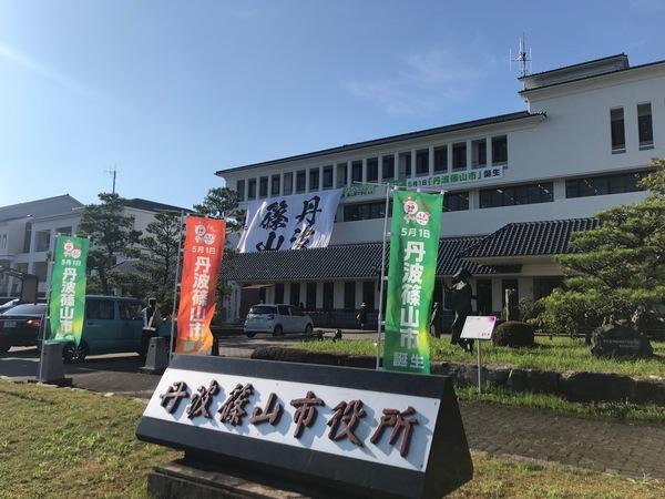 市役所の正面をバックに「丹波篠山市役所」の表札と「丹波篠山市誕生」ののぼり旗が映っている写真