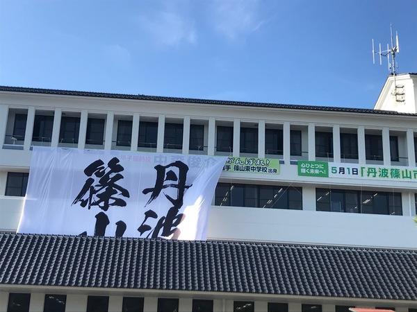 市役所の建物に筆文字「丹波篠山」の大きな長方形の旗が掲げられている写真