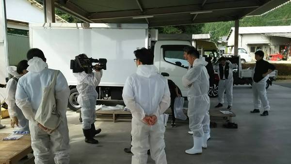 白い防護服を着た男性数名が立っている