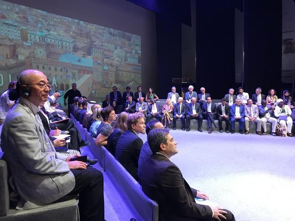 舞台に設けられた席でヘッドホンをつけた市長らが話を聞いている写真