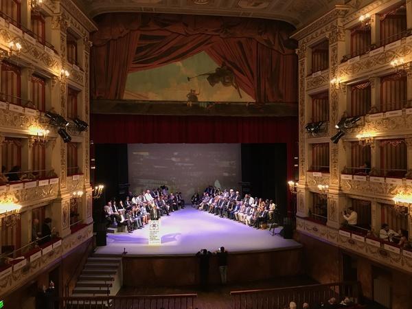 舞台に座っている人々と全体の様子が客席側から撮影されている写真